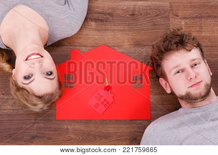 Housing marriage family security future finances mortgage concept. Just married lying on floor. Young man and woman next to home symbol with keyring.