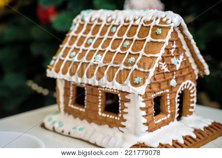 Homemade Christmas Gingerbread House in the snow. Decorated Christmas tree in the background.
