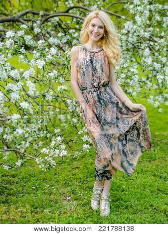 beautiful Russian girl blonde in a summer tight-fitting dress against the background of a blossoming apple tree