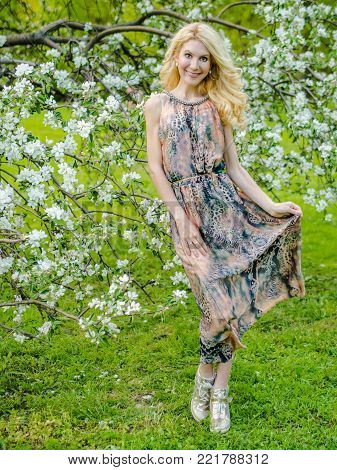 beautiful Russian girl blonde in a summer tight-fitting dress against the background of a blossoming apple tree