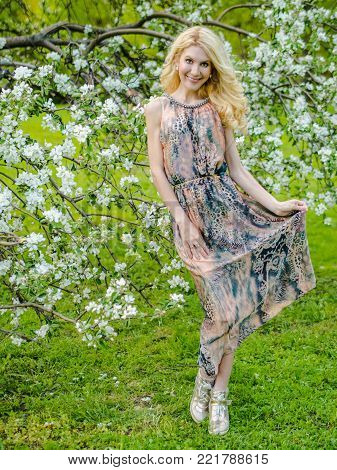 beautiful Russian girl blonde in a summer tight-fitting dress against the background of a blossoming apple tree