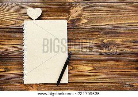kraft paper notepad, pen. wooden heart on wooden background and copy space