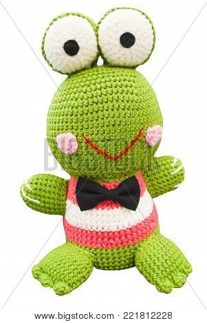 Crochet doll of lovely green frog smiling in Japanesse style with two big eyes on head, pink cheeks, put over shirt in pink and white with black bow tie, isolated white background and clipping path, hobby handmade work with yarn at home for woman