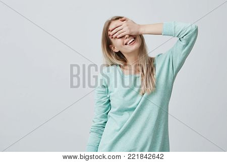 Happy woman with long blonde hair closing her eyes with hand going to see surprise prepared by her boyfriend standing and smiling in anticipation for something wonderful. Young cheerful lady covering her face with hands