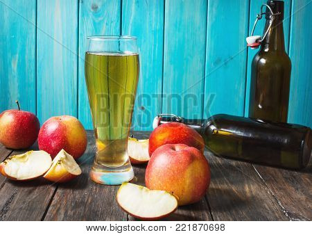 Glass of cider with apples and bottle on rustic wooden background.