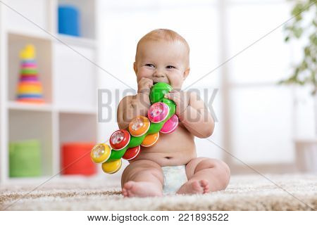 Cute baby in diaper sits on carpet and plays with toy at home. Shallow depth of field.