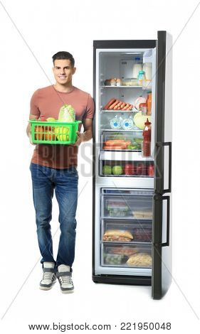 Man with basket standing near refrigerator full of different products, on white background
