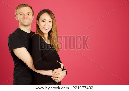 Attractive asian and caucasian inter racial hugging in studio shot against pink background