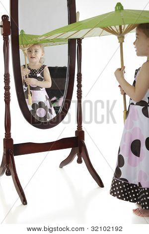 Un'adorabile prescolare con un parasole, controllando se stessa nello specchio.  Concentrarsi sul suo viso in mi