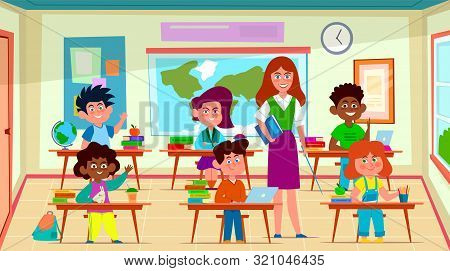 Kids And Teacher In Classroom. School Pedagogue Teaches Lesson To Pupil Group In Class Interior. Edu