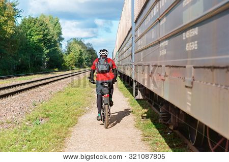 A Man Rides A Bicycle Along The Train, A Cyclist Rides Near The Railway, Kaliningrad Region, Russia,