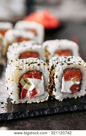 Tokyo salmon uramaki sushi with rice, cream cheese, tomatoes, cucumber, sesame and nori close up. Macro shot of japanese food uramaki rolls with smoked fish and fresh vegetables