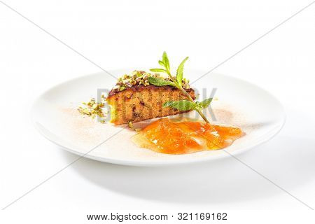 Healthy nut cake with apricot jam isolated on white background. Slice of walnut carrot sponge cake decorated with pistachios and fruit confiture on white round plate for restaurant menu