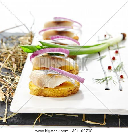 Herring Canape with Potato and Onion on Natural Rustic Background. Beautiful Creative Sea Food Design of Fish Fillet with Scallions on Dry Hay and Black Slate