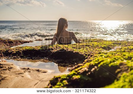 Young Woman Tourist On Pantai Tegal Wangi Beach Sitting In A Bath Of Sea Water, Bali Island, Indones
