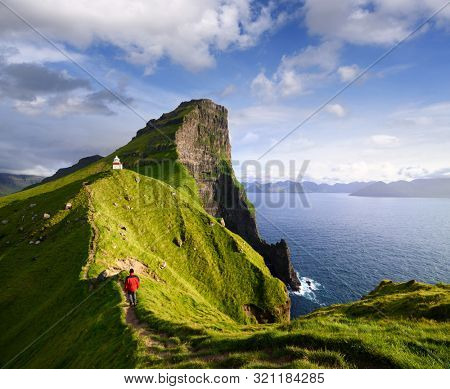 Kallur Lighthouse on Kalsoy island. Hiking on the Faroe islands. Tourist in a red jacket visiting a tourist attraction. Summer mountain landscape