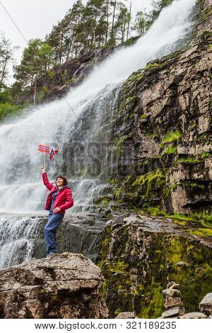 Tourist Woman With Norwegian Flag At Svandalsfossen In Norway, Powerful Waterfall In Norwegian Mount