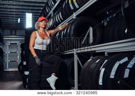 Sexy Woman In Red Cap Is Chilling At Tyre Storage While Posing For Photographer.