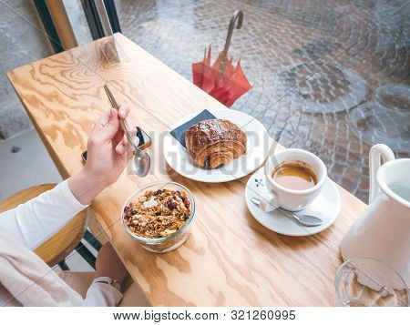 Side Overhead View Of Single Woman Eating Delicious Yogurt With Muesli Drinking Coffee With Croissan