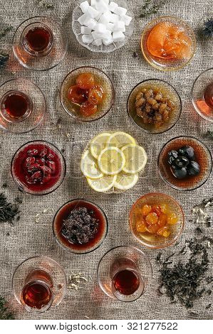Big Collection of Various Homemade Jam or Pozzy with Tea and Sliced Lemon on Rustic Tablecloth Burlap Background Top View. Cornus Mas Confiture, Apricot Jelly, Grape, Plum and Apple Marmalade Set