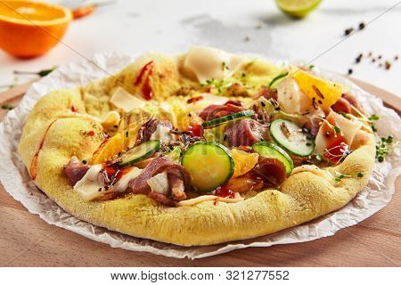 Pita with duck fillet and vegetables on craft paper and wood plate closeup. Macro shot of freshly baked yeast round flatbread with sliced goose fillet, melted cheese, cucumbers, tomatoes and spices