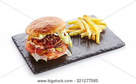 Fresh Beef Burger with Bacon, Fried Onions, Tomato Sauce, Pickled Cucumbers, Green Lettuce, Cheese and French Fries Garnish. Hamburger or Beefburger on Natural Black Stone Plate Isolated on White
