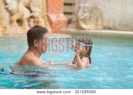 Senior Asian Man Is Enjoying Time With Him Adorable Three Year Old Grandchild In A Swimming Pool, Ha