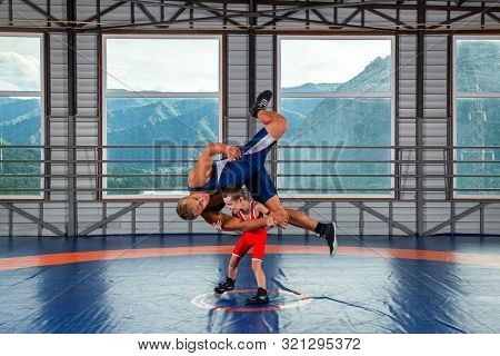 A  Wrestler Boy In A Sports Tights Wrestles With An Adult Male Wrestler On A Wrestling Carpet In The