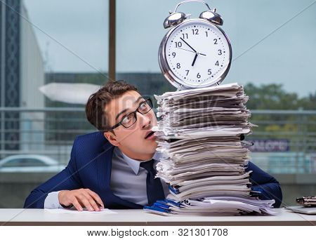 Businessman with pile stack of paper paperwork and an alarm cloc