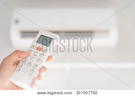 Woman Hand Holding Remote Controller Directed On The Air Conditioner Inside The Room And Set At Ambi