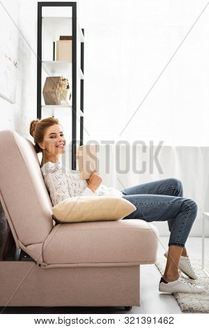 Attractive Woman In White Sweater Holding Book And Looking At Camera