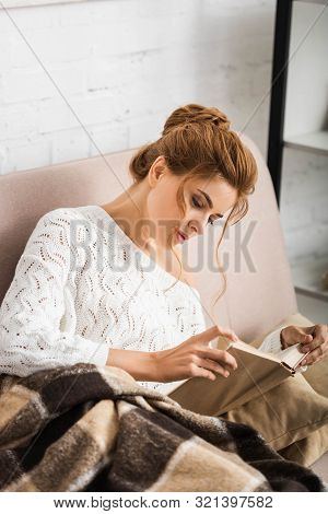 Attractive Woman In White Sweater Sitting On Sofa And Reading Book
