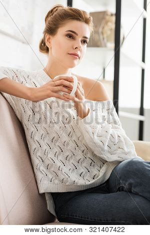 Attractive Woman In White Sweater Holding Cap And Looking Away
