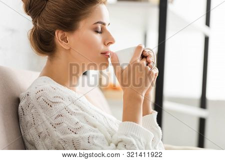 Side View Of Attractive Woman In White Sweater Holding Cup