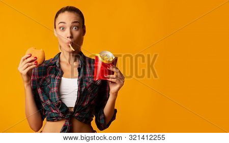Oops, Cheat Meal. Surprised Millennial Girl Eating Burger And French Fries On Yellow Studio Backgrou