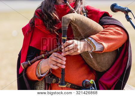 Musician In Medieval Clothes Performs A Melody On A Bagpipe