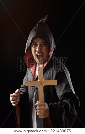 Male Exorcist In Black Coat Holding Crucifix To Exorcise Ghost On Black Background