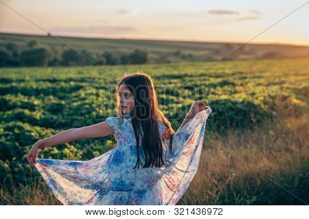 Calmy Beautiful Brunette Teen Girl With Loose Hair Atanding Among The Mealow, Holding Flying Dress W