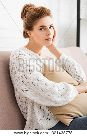 Attractive Woman In White Sweater Holding Pillow And Looking At Camera