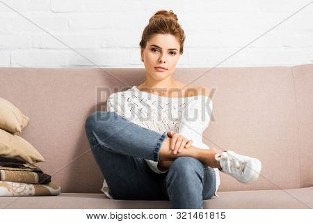 Attractive Woman In White Sweater Looking At Camera And Sitting On Sofa