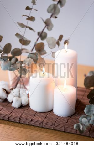 decoration, hygge and cosiness concept - burning white candles, branches of eucalyptus populus and cotton flowers on table