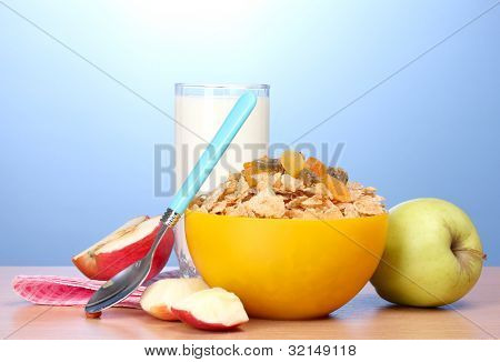 leckere Cornflakes in gelbe Schale, Äpfel und Glas Milch auf Holztisch auf blauem Hintergrund