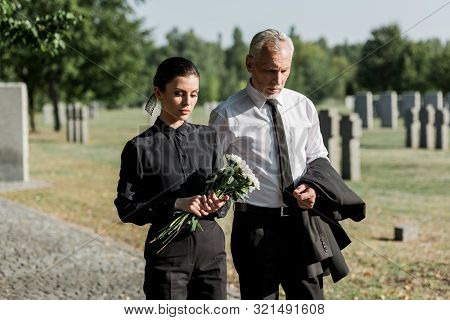 Bearded Senior Man Walking Near Woman With Flowers On Funeral