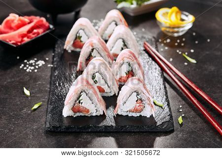 Macro shot of bacon uramaki sushi rolls with rice, cream cheese, smoked salmon, pork lard, cucumber, green onions, nori. Sushi rolls with chopsticks in Japanese restaurant closeup