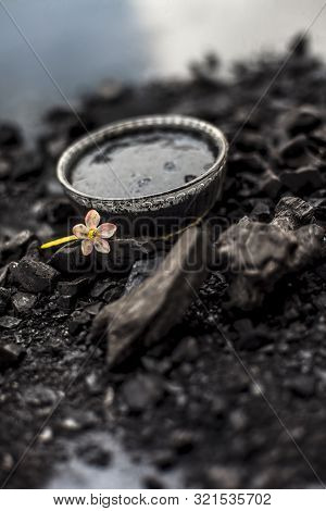 Close Up Of Activated Charcoal In A Glass Bowl On The Wooden Surface Along With Some Raw Powder Of C