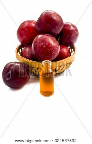 Raw Organic Red Ripe Plums In A Brown-colored Basket Along With Its Extracted Essential Oil In A Sma