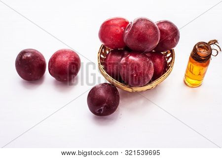 Raw Organic Red Ripe Plums In A Brown-colored Basket Along With Its Extracted Essential Oil In A Tra