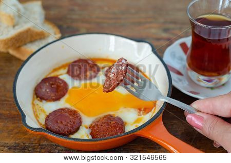 Turkish Breakfast With Fried Egg,  Sucuk And Turkish Tea On Wooden Table. The Woman Is Eating Sucuk.