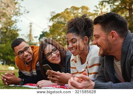 Group Of Happy Diverse Friends Looking At African American Woman Using Her Mobile Phone In The Park 