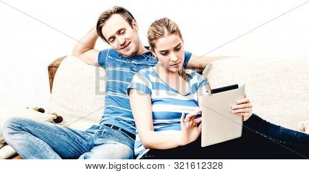 Cuople browsing news in tablet while sitting on sofa in living room. Home internet.